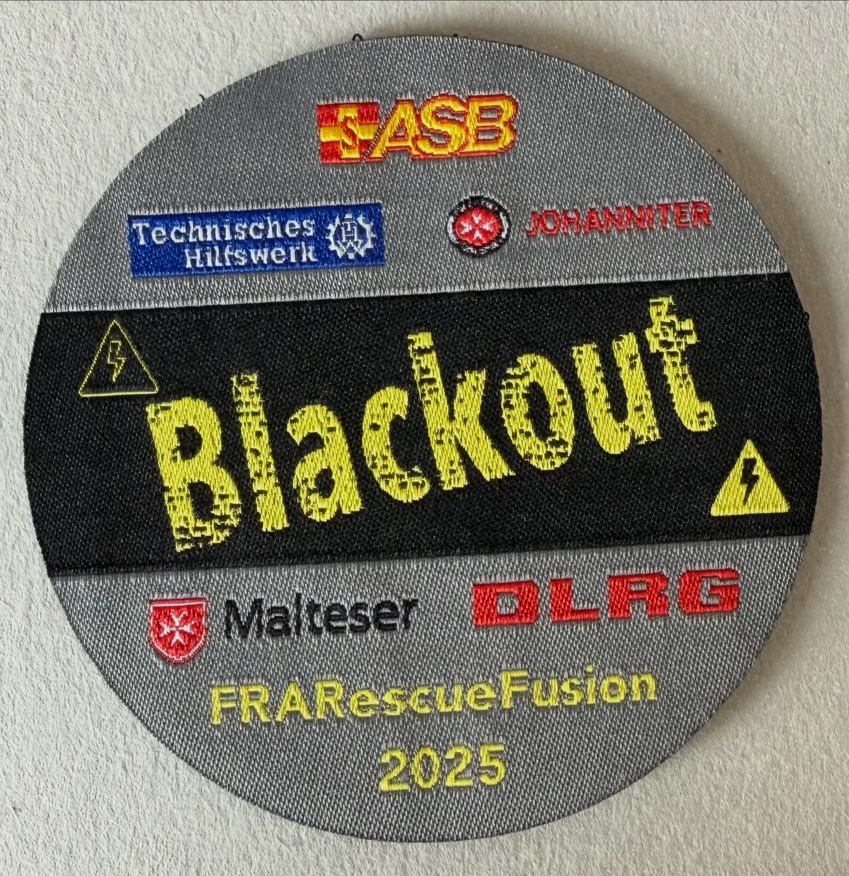Grauer Blackout-Patch der FRARescueFusion 2025 mit Logos der Hilfsorganisationen